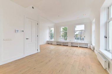 Boş bir oturma odası, ahşap döşeme ve evin önündeki sokağa bakan büyük pencereli.