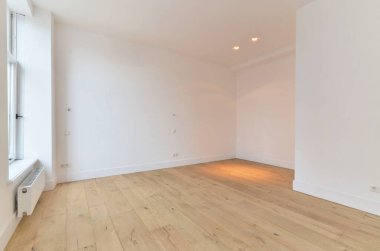 Beyaz duvarları ve sağ tarafında ahşap döşemeleri olan boş bir oda. Köşede bir ısıtıcı var.