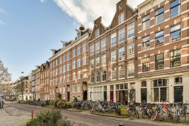 Bazı bisikletler caddenin kenarına park edilmiş. Bir sürü penceresi olan tuğlalı binaların önünde.