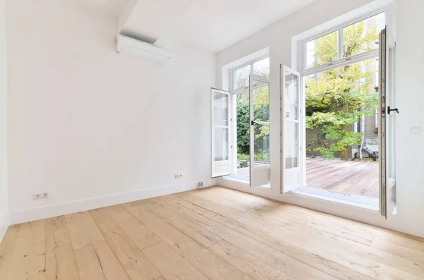 stock image an empty room with white walls and wood flooring, looking out onto the garden from the living room door