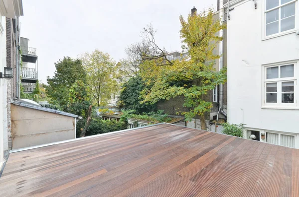 a wooden deck with trees in the back ground and buildings on either side, taken from inside to outside view