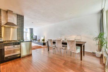 Ahşap döşemeleri, paslanmaz çelik aletleri ve beyaz duvarları olan modern bir oturma odasında mutfak ve yemek odası.