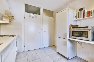 Beyaz dolaplı bir mutfak ve odanın kapısının önündeki tezgahta bir fırın boş.