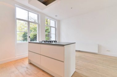 Bu odadaki beyaz dolapları ve siyah tezgahları olan boş bir mutfak çok hafif ahşap döşemedir.