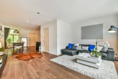 Tahta döşemeleri ve beyaz halıları olan bir oturma odası. Kanepelerin önünde, ahşap zeminde.