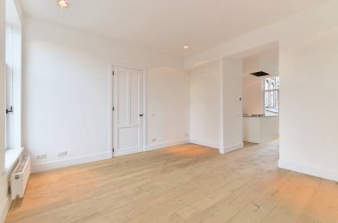 Odasında ahşap döşeme ve beyaz duvarlar olan boş bir oturma odası çok temiz, ama mobilya yok.