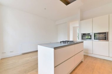 Beyaz dolaplı bir mutfak ve tezgahın önündeki duvarda ahşap döşemeli bir fırın.