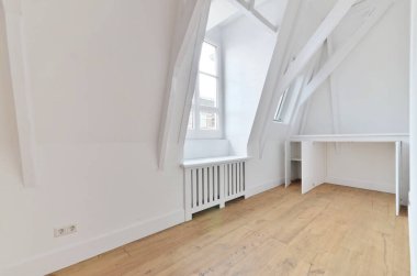 Beyaz duvarları ve sağında ahşap döşemeleri olan boş bir oda, solda bir pencere var.