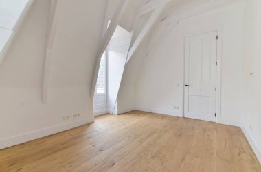 Beyaz duvarları ve sağında ahşap döşemeleri olan boş bir oda. Başka bir odaya açılan bir kapı var.