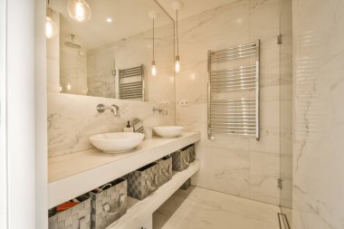 Mermer duvarları ve beyaz tezgahları olan modern bir banyo. Duvardaki iki lavabo da camdan yapılmış.