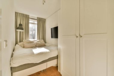 Köşesinde yatak ve dolap olan küçük bir oda. Duvarında bir televizyon var.