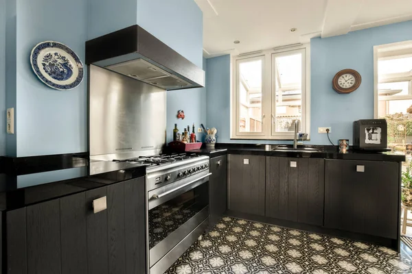 a kitchen with blue walls and white trim around the stove, black cabinetry and counters on either sides