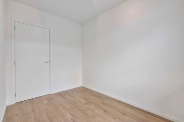 Ahşap zemini ve beyaz duvarları olan boş bir oda. Odanın sol tarafına açılan bir kapı var.