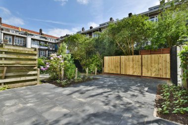 Etrafı ağaçlarla çevrili bir apartmanın önünde çitleri ve bitkileri olan bir arka bahçe.