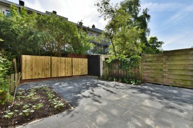 Resimde ahşap çitleri ve yeşil ağaçları olan bir arka bahçe alanı bir açıdan yere doğru çekiliyor.