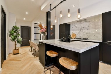 Mermer tezgahlı bir mutfak ve odanın ortasında ahşap tabureler, adada bir bitki var.