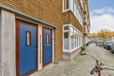 Mavi kapılı ve pencereli tuğla bir binanın önündeki caddenin kenarına park etmiş bir bisiklet.