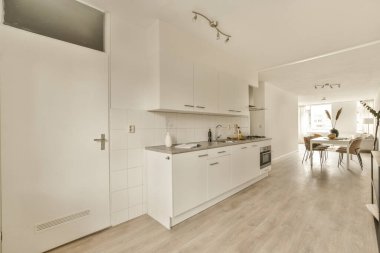 Beyaz dolapları, ahşap zemini ve oturma odasına açılan kapısı olan bir evde mutfak ve yemek odası.