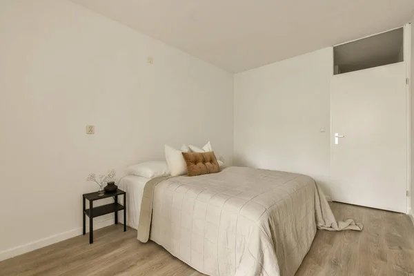 有白色墙壁和木制地板的卧室 包括房间中央的一张大床 是一张黑色的小桌子 — 图库照片