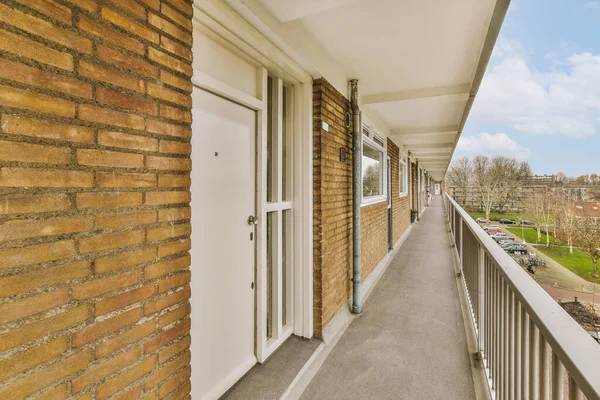 a balcony with brick walls and white trim on the outside wall, looking out onto the street from an apartment