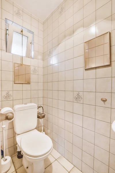 浴室里有一个白色的马桶 地板上有瓷砖 后面有墙 马桶上方有一面镜子 — 图库照片