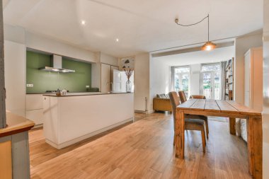 Ahşap döşemeli, beyaz duvarlı ve yeşil aksanlı duvar kağıtlı bir evde mutfak ve yemek odası.