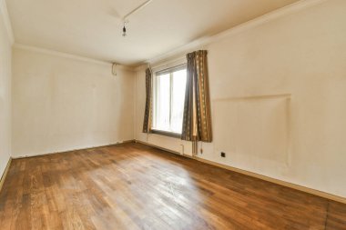 Ahşap döşemeleri ve beyaz duvarları olan boş bir oturma odası var. Sokağa bakan bir pencere var.