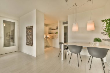 Tavanda beyaz duvarlar, ahşap döşemeler ve lambalar olan bir evde mutfak ve yemek odası.