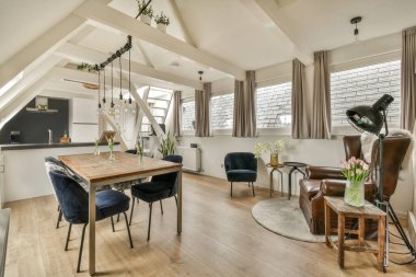 Ahşap zemin ve beyaz duvarları olan bir oturma odası. Ortasında iki mavi sandalye ve ahşap bir masa var.