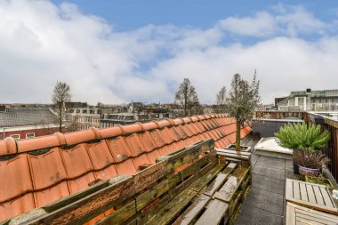 Gökyüzü ve bulutlar eski ahşap banklar, bitkiler ve çömlekler ile kentsel bir alanda bazı çatılar üzerinde