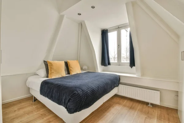 a bed in a room with white walls and wood flooring on one side, there is a blue blanket on the other side