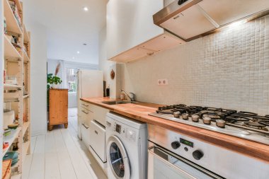 Sobanın üstünde beyaz fayanslar, ahşap tezgah, fırın ve köşede bulaşık makinesi olan bir mutfak.