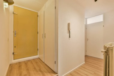 Ahşap zeminli boş bir oda ve aynı bölgede başka bir odaya açılan sarı kapı.