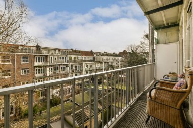 Güneşli bir günde, arka planda bir sandalyenin ve bazı binaların olduğu bir balkon.