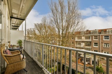 Ön planda sandalye ve ağaç olan bir balkon, bir apartmanın çatı terasından alındı.