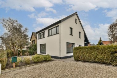 Etrafında çalılar ve ağaçlar olan bir evin ortasında mavi bir gökyüzü var.