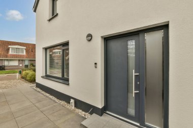 Gri kapıları ve pencerelerinde siyah panjurları olan, sokağa bakan bir evin dış görüntüsü.