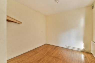 Ahşap döşemesi ve duvarlarında beyaz duvar kağıdı olan boş bir oda yukarıdan çekilmiş.