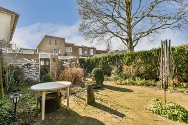 Her iki tarafında bitki ve ağaçlarla çevrili arka bahçesinde bir masa ve sandalyeler var. Mavi bir gökyüzü var.