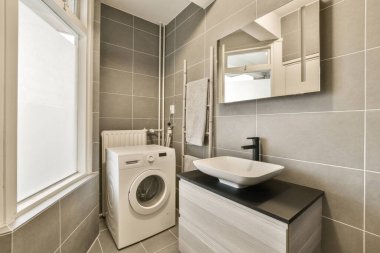 Köşesinde çamaşır makinesi ve kurutma makinesi olan bir çamaşır odası duvarında bir aynanın yanında.