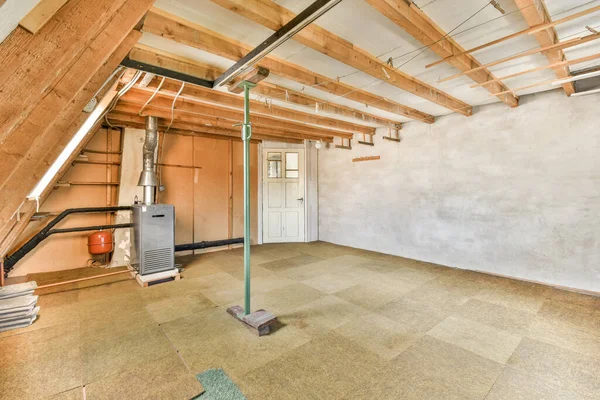 天井に木製の梁とその下の床に壁を走るパイプが露出した未完成の部屋 — ストック写真