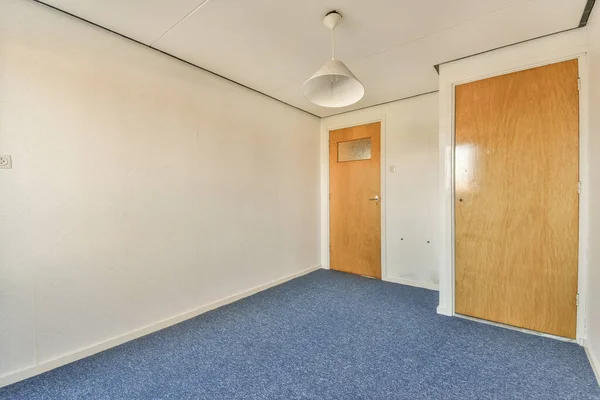 ドアの前の床に木製のドアと青いカーペットがある空の部屋は白い壁です — ストック写真