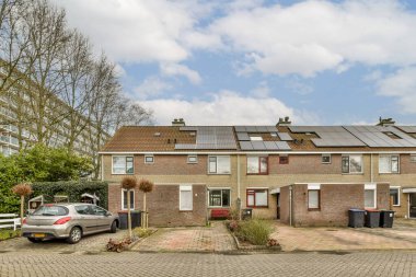 Çatıda güneş panelleri olan bir ev ve önünde kameradan uzak duran iki araba.