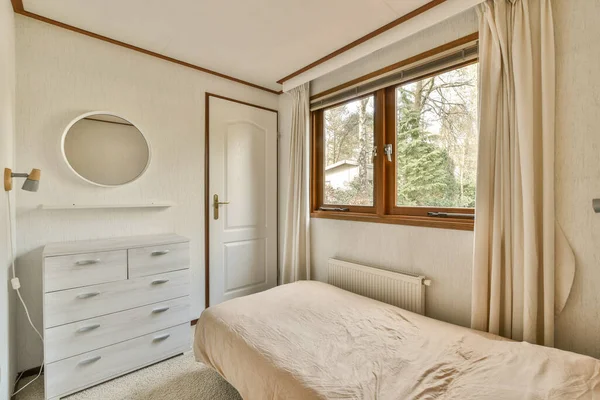 a bedroom with a bed, dresser and large window looking out onto the trees outside in the photo is taken from inside
