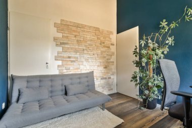 Kanepenin yanında kanepesi, sandalyesi ve bitkisi olan bir oturma odası tuğla bir duvardır.