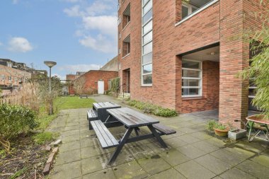 Bir bankı olan bir dış alan ve kırmızı tuğlalı binanın önünde bazı bitkiler vardı.