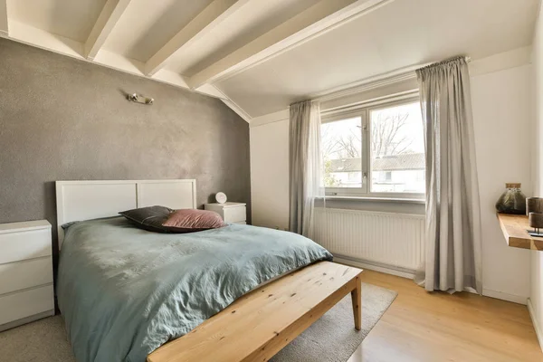 房间中央有一个有床 窗户和木制长椅的卧室 墙上有一盏灯 — 图库照片