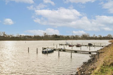 Bazı tekneler güneşli bir günde mavi gökyüzü ve gölün üzerinde tüylü beyaz bulutlarla suya yanaştılar.