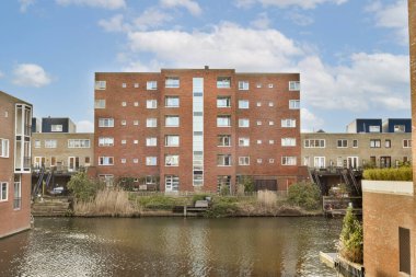 Birçok penceresi olan tuğla bir binanın önündeki su birikintisinin yanındaki bazı binalar.