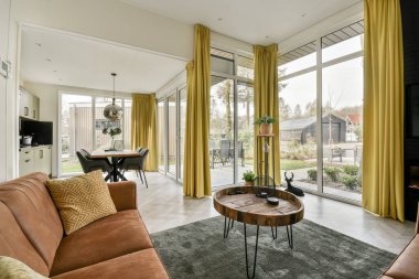 Oturma odası, iki kanepe ve pencerenin önünde bir sehpa. Arka bahçeye bakıyor.